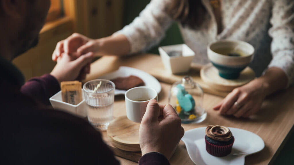 a couple holding hands at a table with dishes of food, resolving conflict