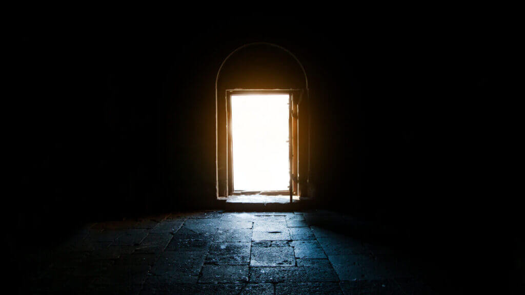 a dark room with a doorway illuminating light into the entrance