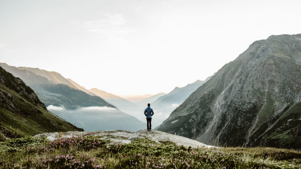 man standing on the edge of a mountain looking at the grand view below