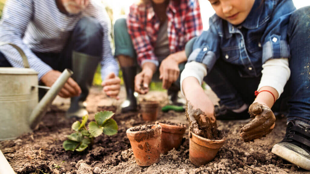 a family kneels in soil and fills pots with their hands, faith and failure