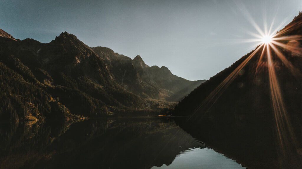 view of mountains beyond a body of water with the hint of the sun coming over the mountains