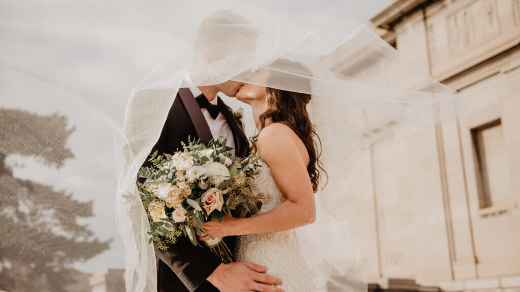 a newly married couple kissing under the bride's veil 