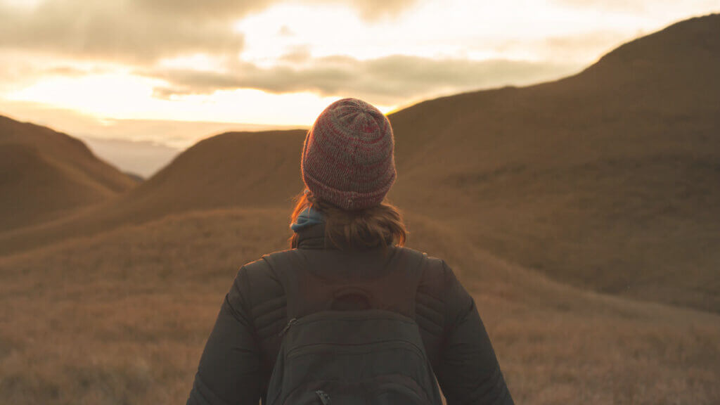 a woman wearing a beanie facing a mountain range