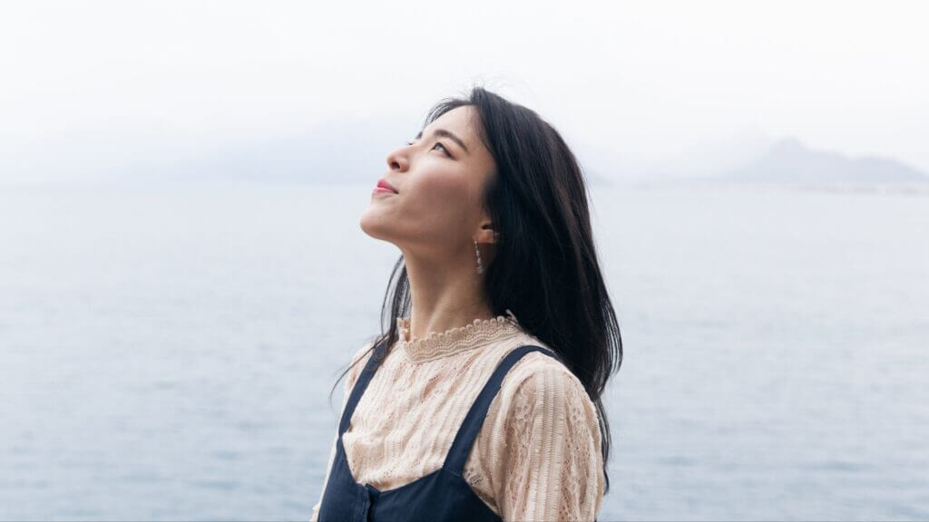 a woman with dark hair with her face turned upwards toward the sky