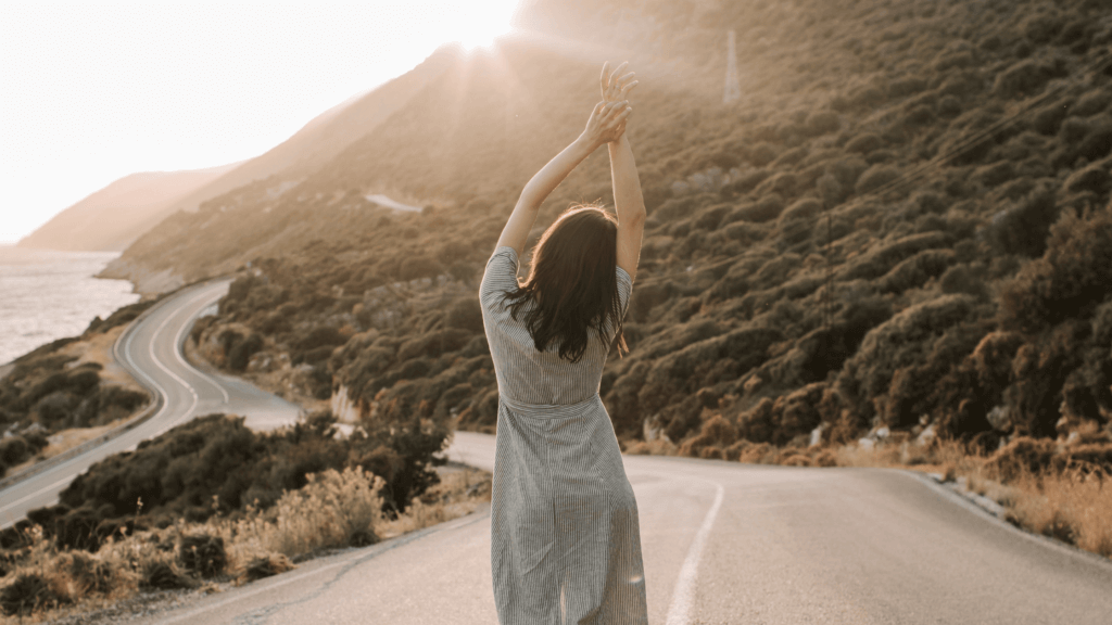 the back view of a woman walking along a road with her hands up over her head