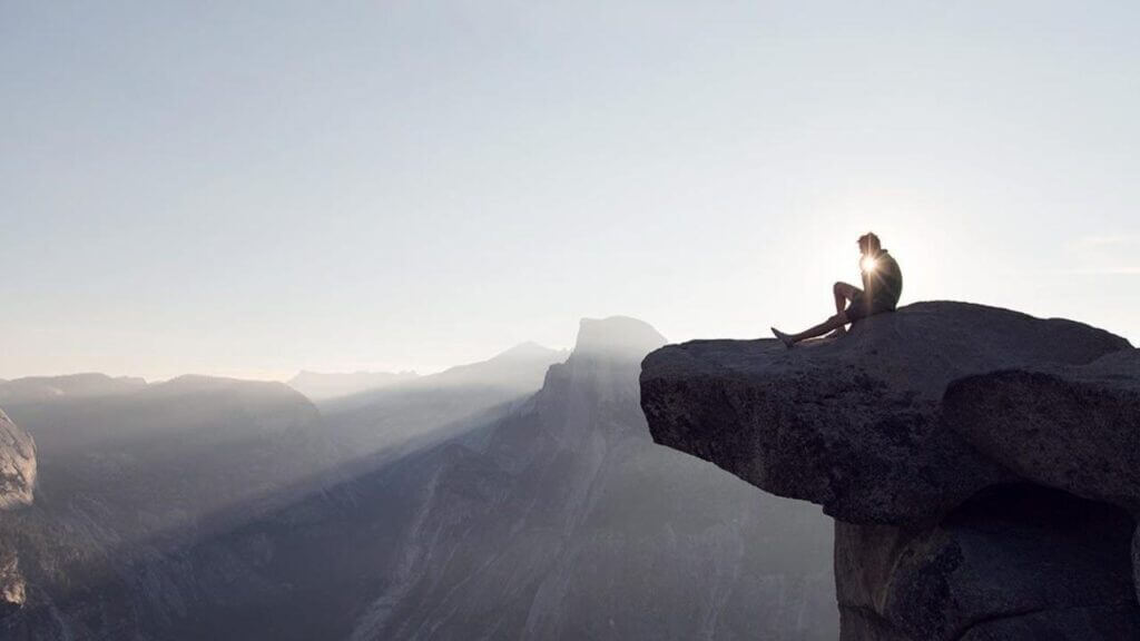 a person sitting on a rock looks out on the vast view below them catholic psychology