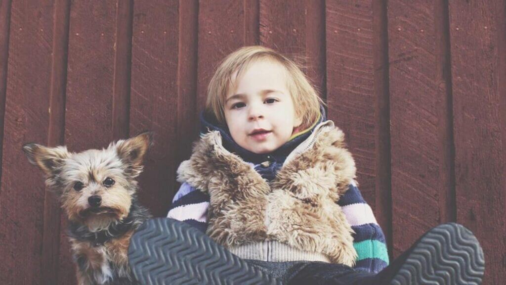 a small boy leans back against a wall with a small dog sitting next to him, being present with your children