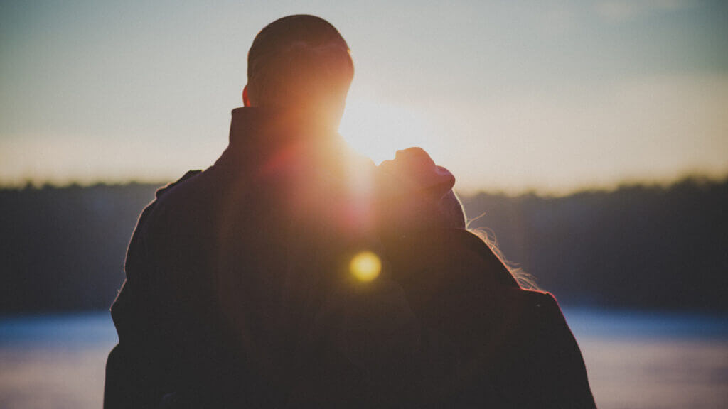 man and woman leaning against each other watching a sunset