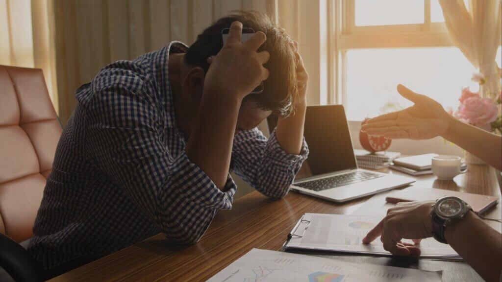 a man sitting at a desk holds his hands up to his head in frustration manage stress