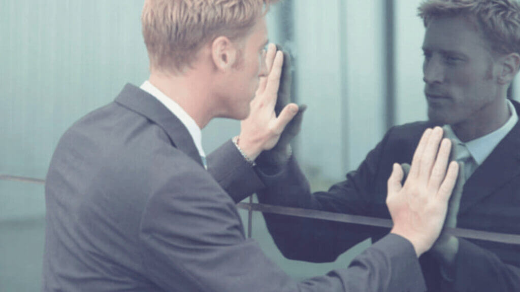 man looks at his own reflection from a building healing