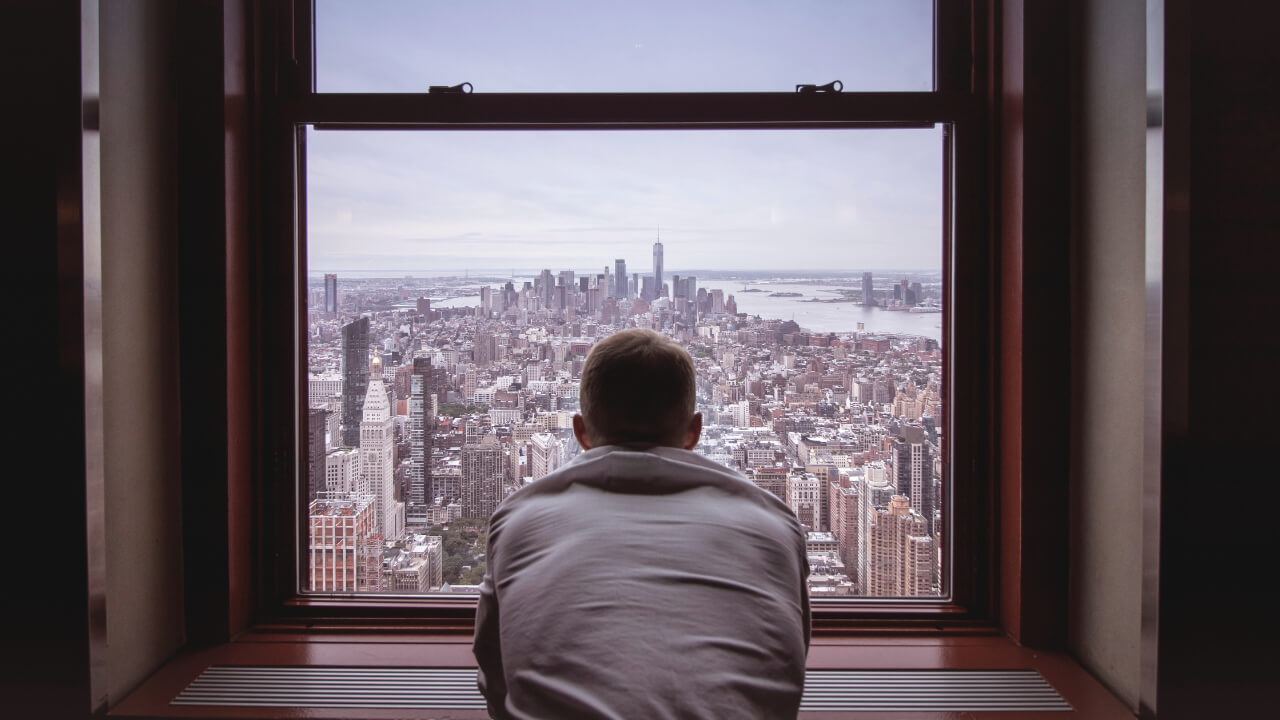 man looking out of a window at a view of a city feel less stressed
