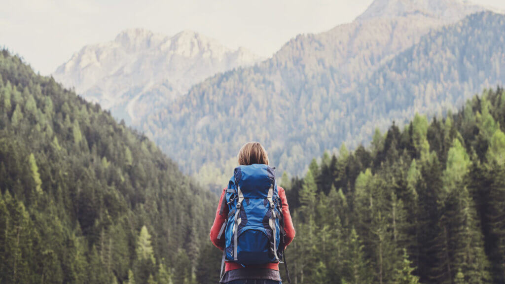 woman facing a mountain seen with green trees, one thing to do when you feel overwhelmed