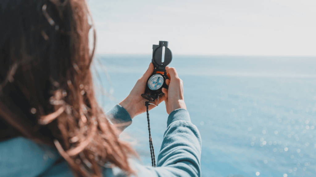 a woman holding a compass as she faces a body of water Catholic guilt