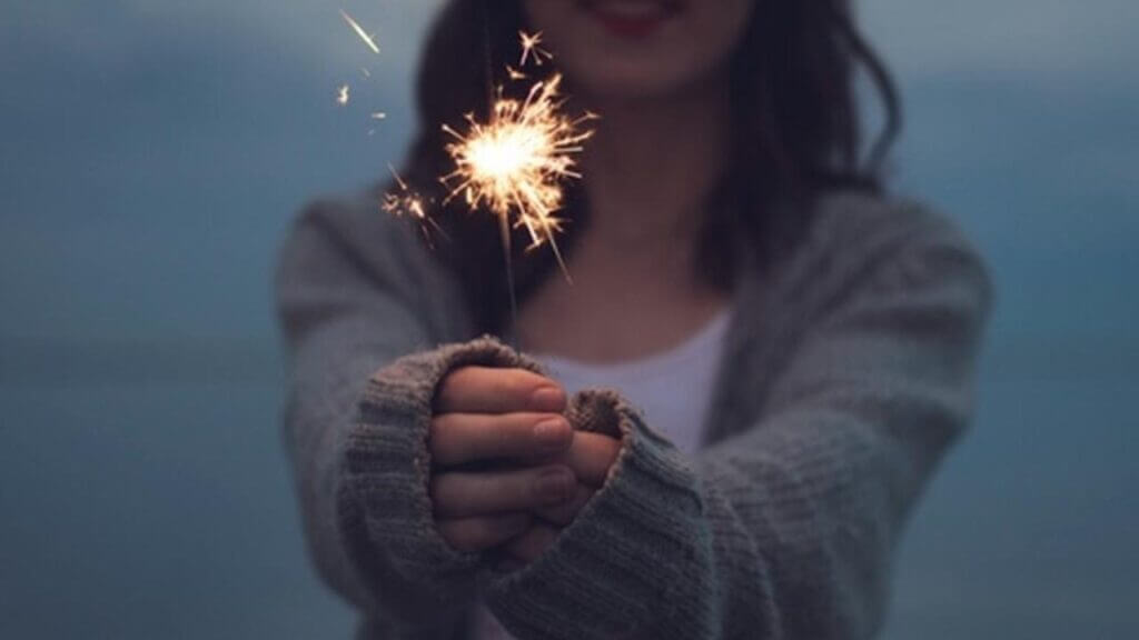 a woman holding a lit sparkler in front of her, win at new year's resolutions