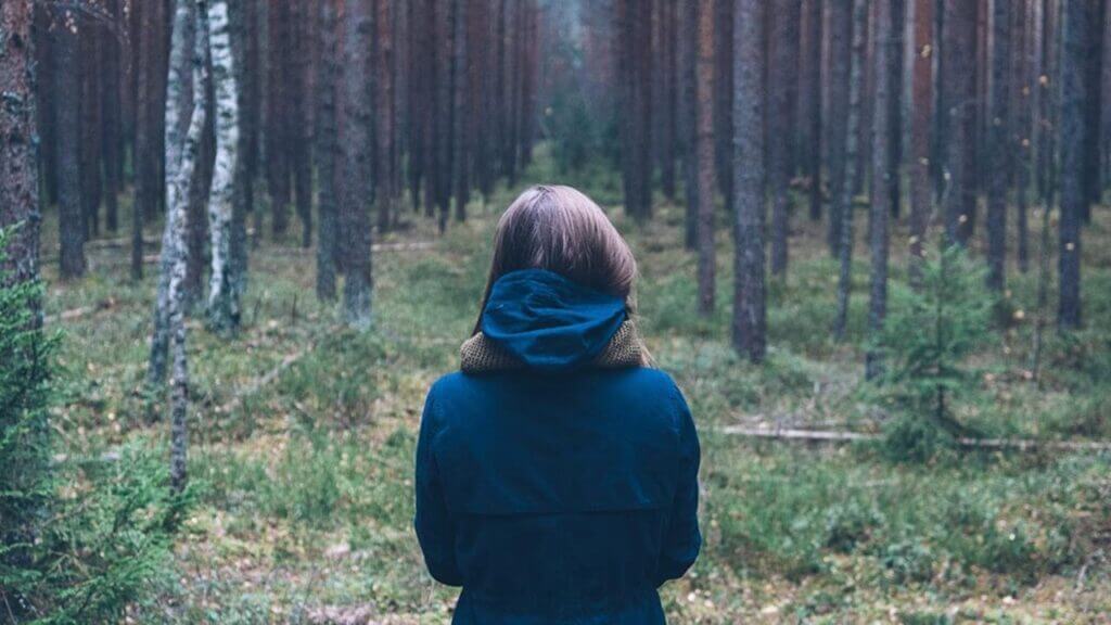 woman dressed in dark blue facing a forest crowded with trees, living a faithful life