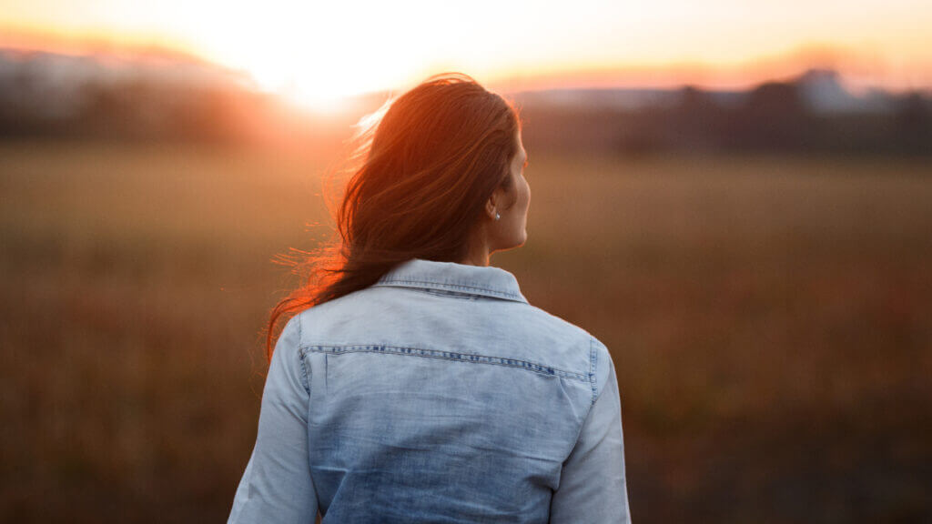 back of woman looking at a field at sunset worry