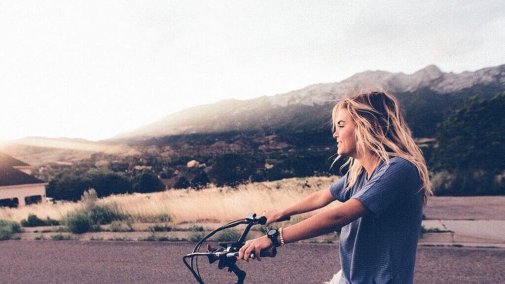 a young woman on a bike with mountain behind her - virtue