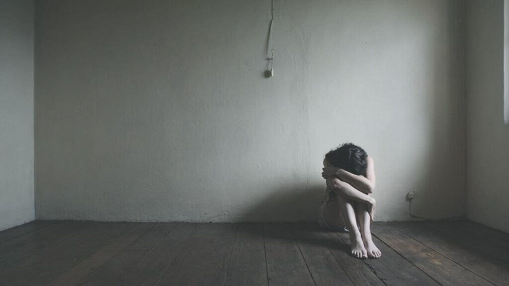 a woman on the floor in a bare room hugging her knees to her chest, abortion hurts women